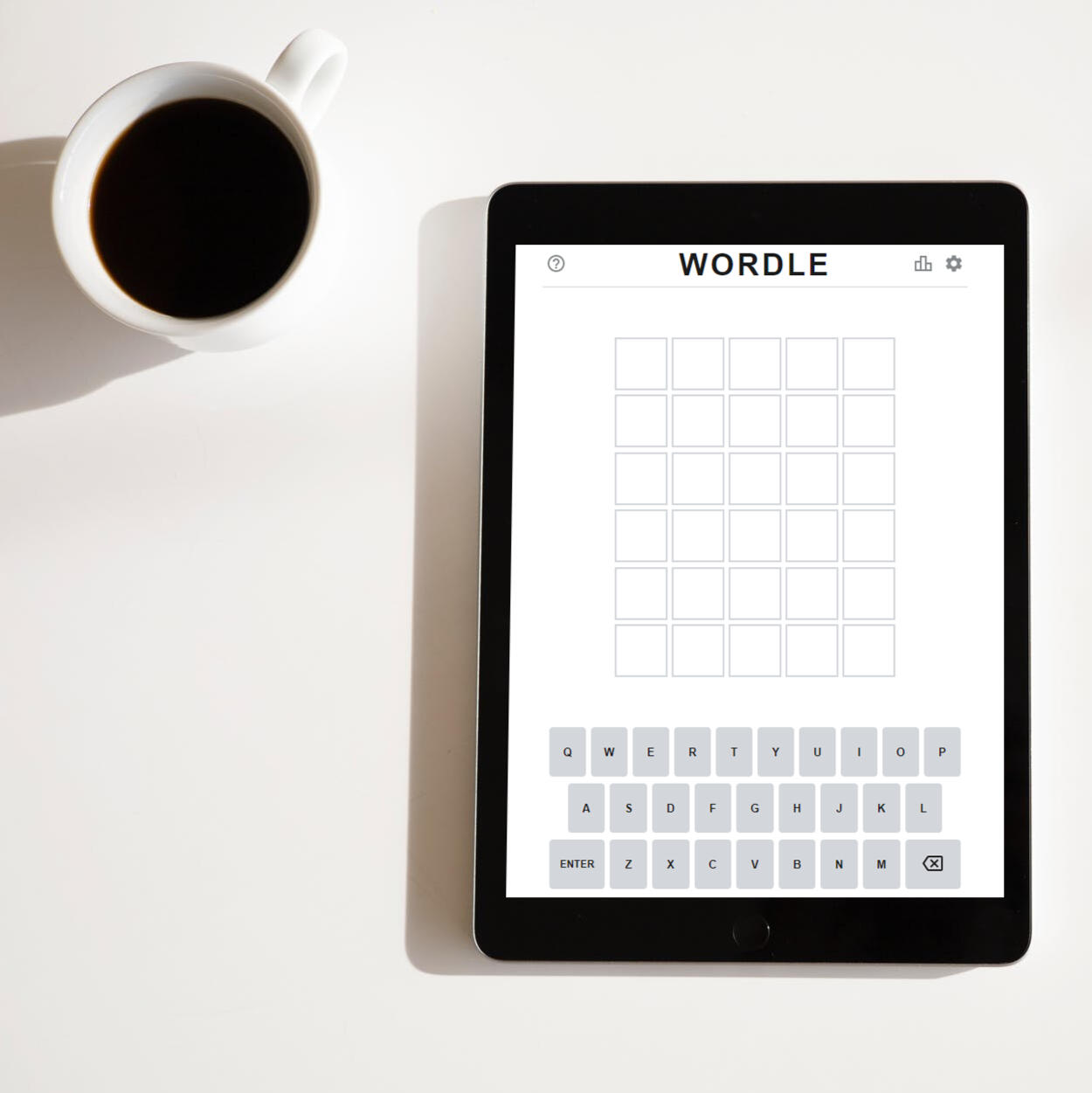 Picture of an iPad next to a cup of coffee, on top of a white table. The iPad screen shows the Wordle website.